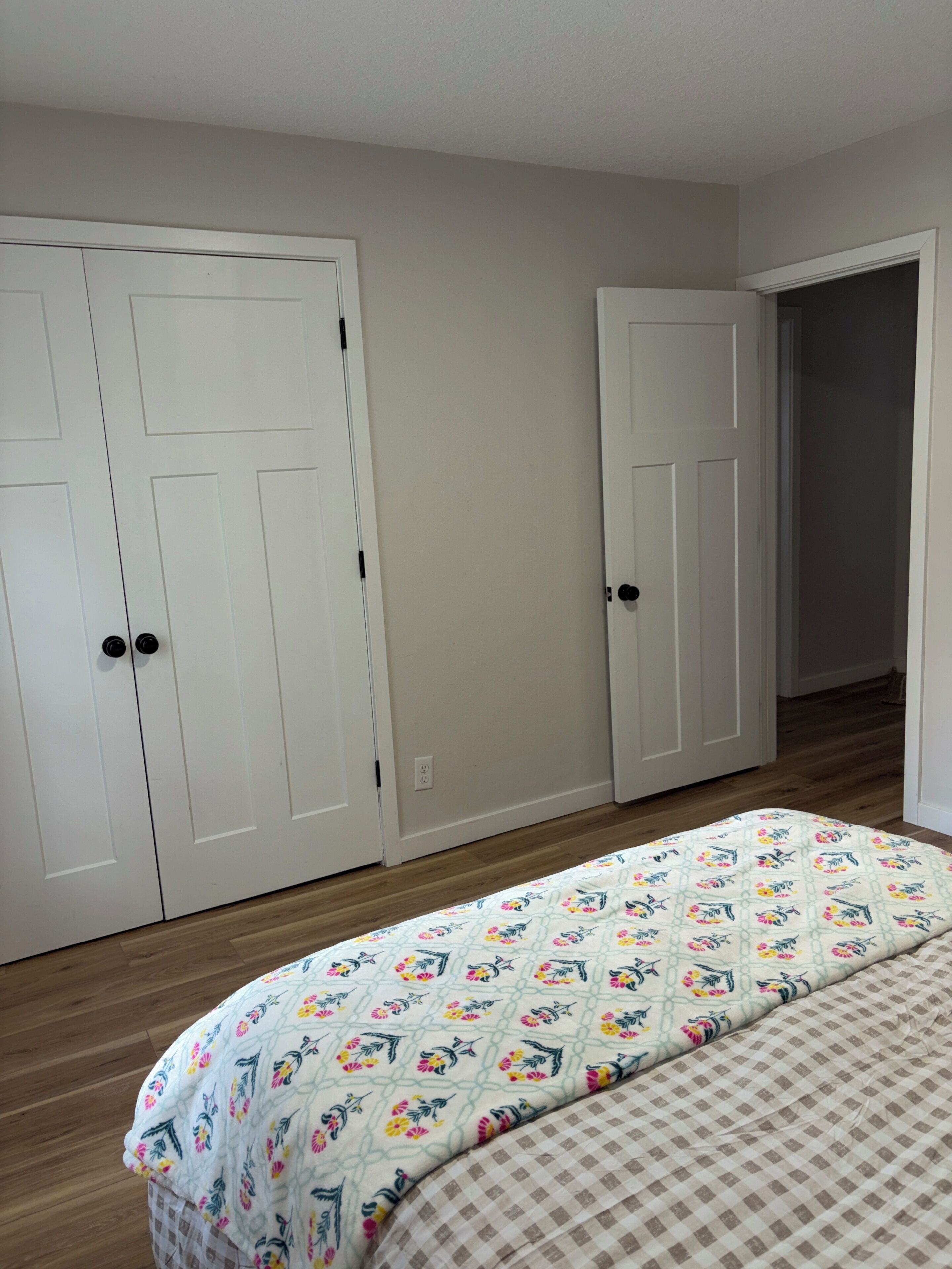 A bedroom with a bed, two white doors, and a wooden floor.