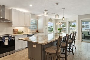Een moderne keuken met een groot eiland, roestvrijstalen apparatuur en hanglampen.