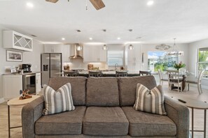 A modern kitchen with white cabinets, a stainless steel refrigerator, and a dining area with a table and chairs. - Isle Be Back: New! Walk to Beach/Times Square/Margaritaville, 2 King Suites! (Fort Myers Beach)