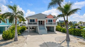 A two-story house with a balcony, palm trees, and a clear sky. - Isle Be Back: New! Walk to Beach/Times Square/Margaritaville, 2 King Suites! (Fort Myers Beach)