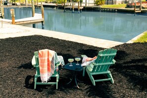 Two green Adirondack chairs with a table and two drinks, set on a patio with a pool in the background. - Isle Be Back: New! Walk to Beach/Times Square/Margaritaville, 2 King Suites! (Fort Myers Beach)