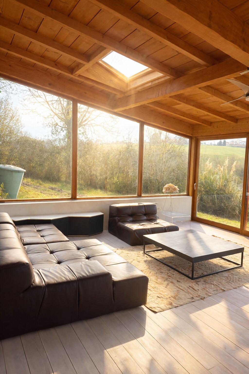 Een modern interieur met een houten plafond, grote ramen, een hoekbank, een bijzettafeltje en een hanglamp.