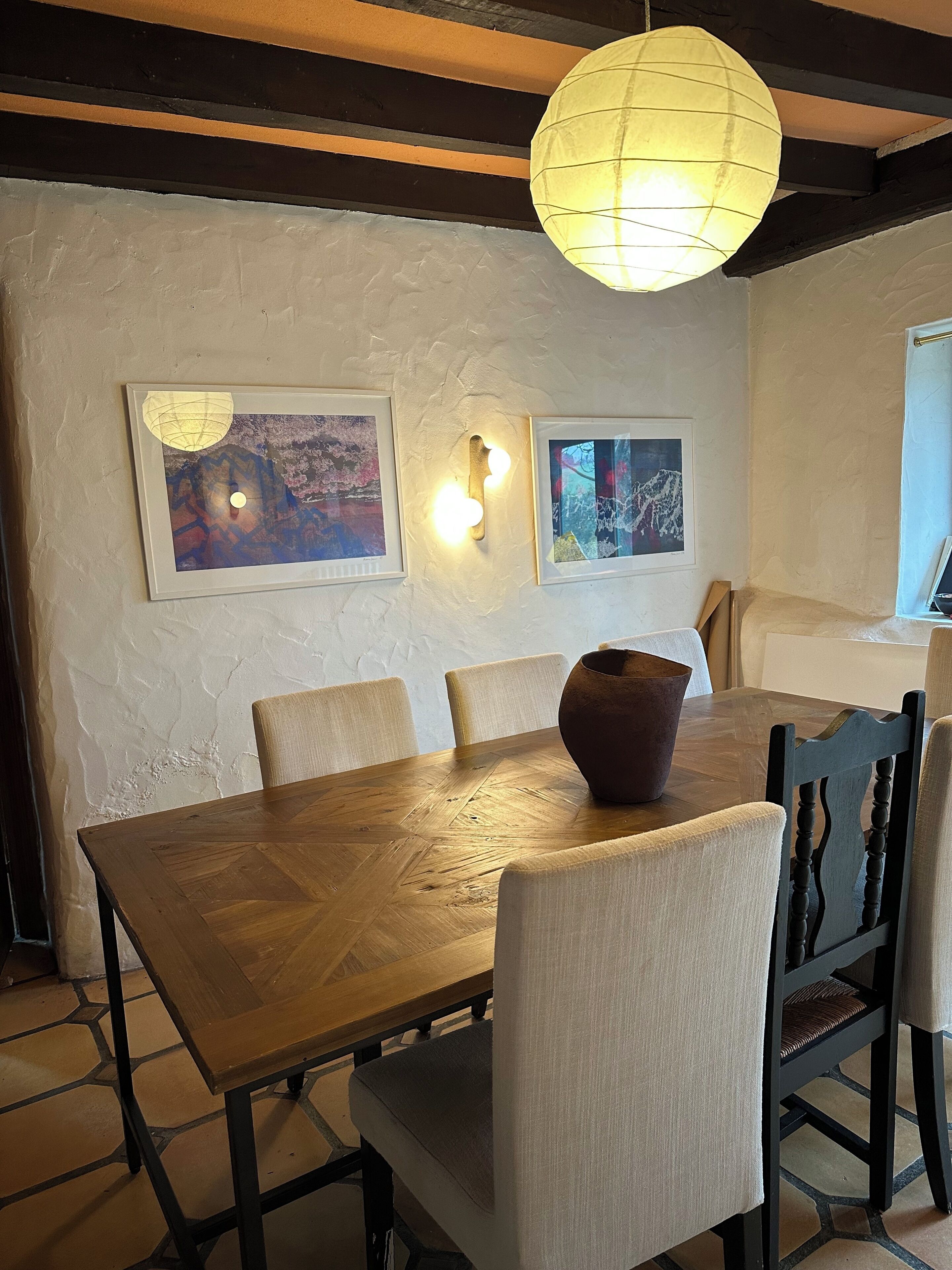 Een eetgedeelte met een houten tafel, vier stoelen, een grote vaas en wandlampen.