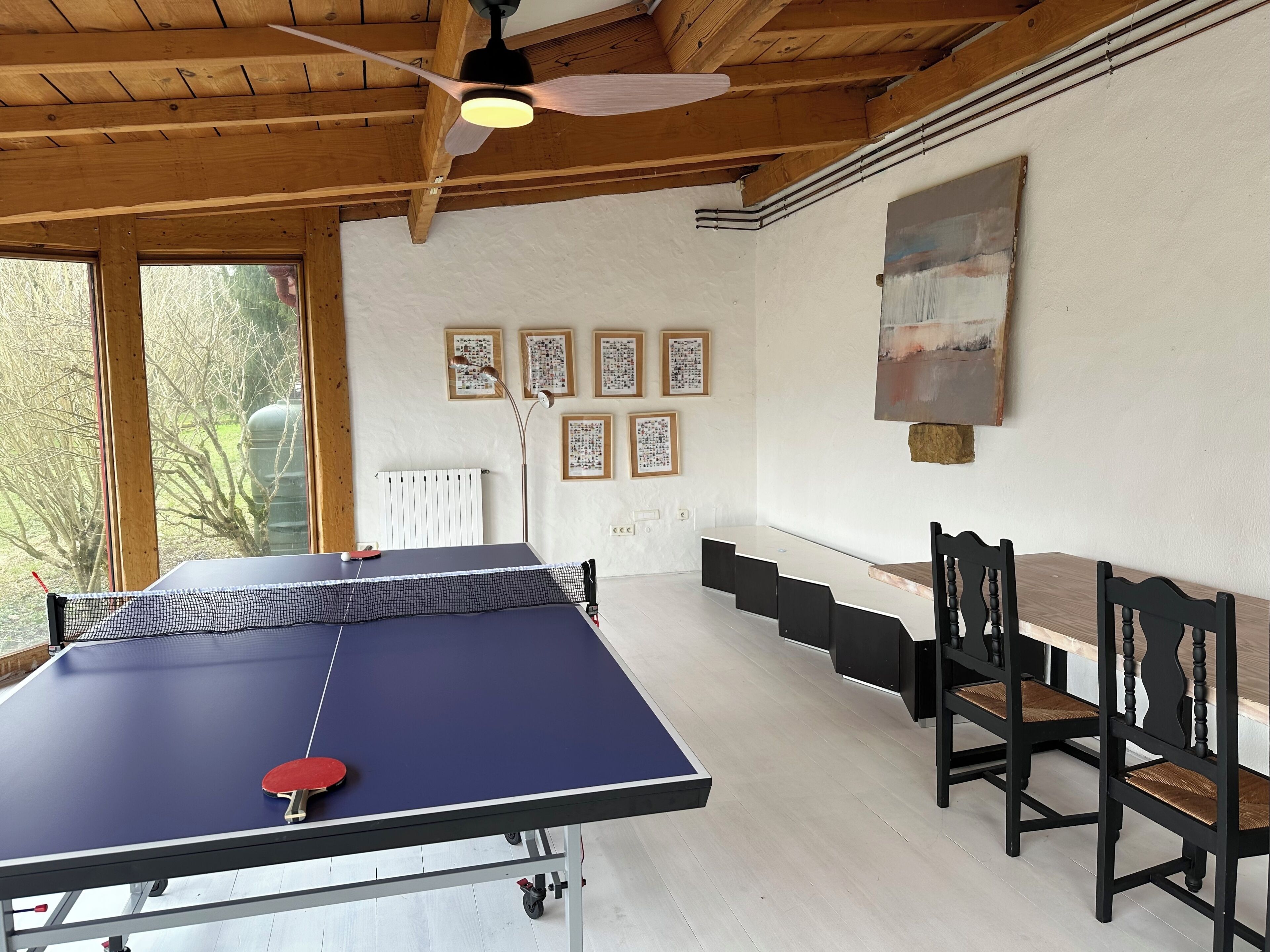 Une table de ping-pong avec des chaises, un ventilateur de plafond et des œuvres d’art accrochées au mur.