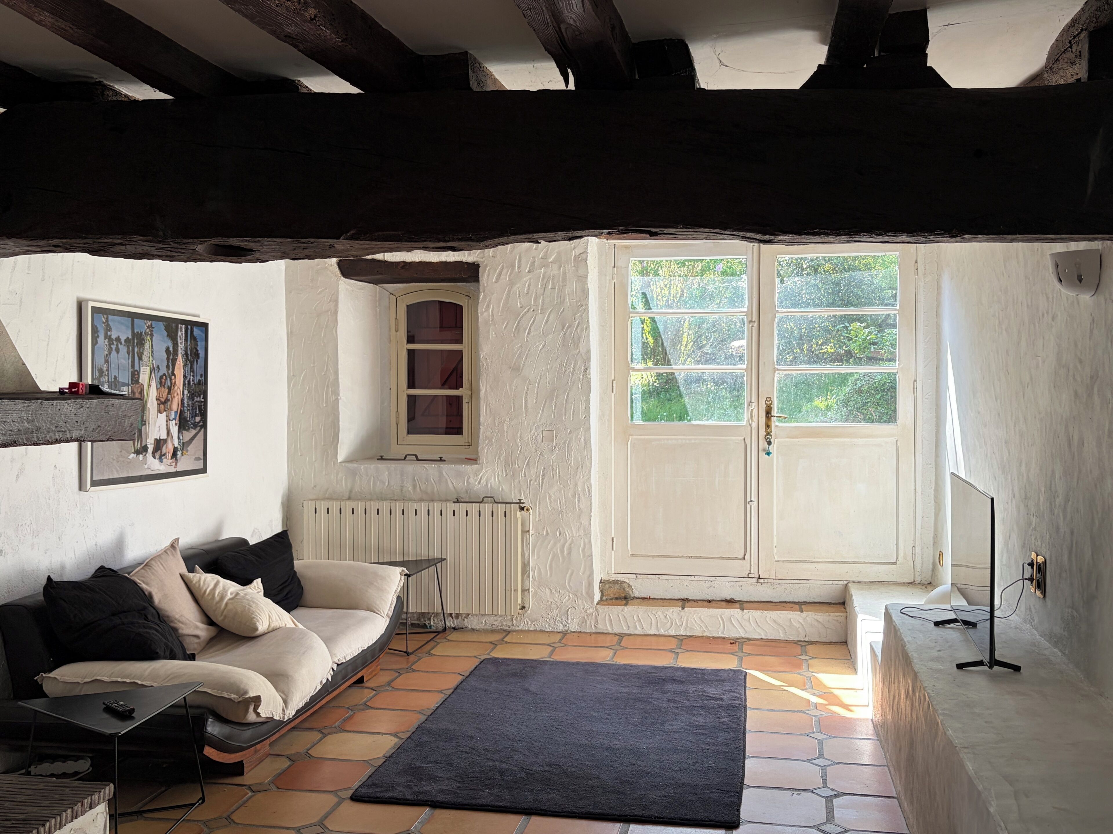 Une pièce confortable avec un canapé, une petite table, un radiateur, une fenêtre donnant sur un espace verdoyant et une porte.
