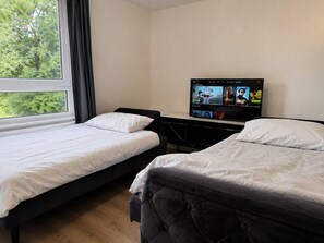 Habitación de hotel con dos camas, un televisor en la pared y una ventana con cortinas.