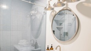 Une salle de bain moderne avec une douche à parois de verre, un miroir rond et un meuble-lavabo en marbre.