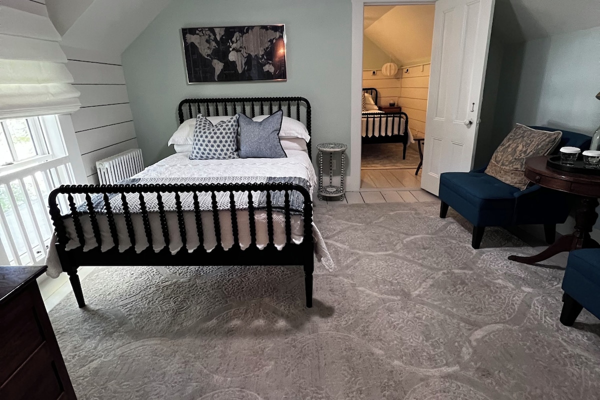 Ein Schlafzimmer mit einem Bett, einem Deckenventilator, einem Heizkörper, einem kleinen Tisch und einem Sessel.
