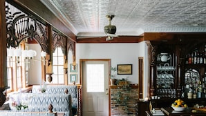 Une pièce spacieuse dotée d’un plancher en bois, d’un coin salon avec des meubles recouverts d’un tissu à motifs, d’un bar avec des étagères remplies de bouteilles et d’un plafond décoratif.