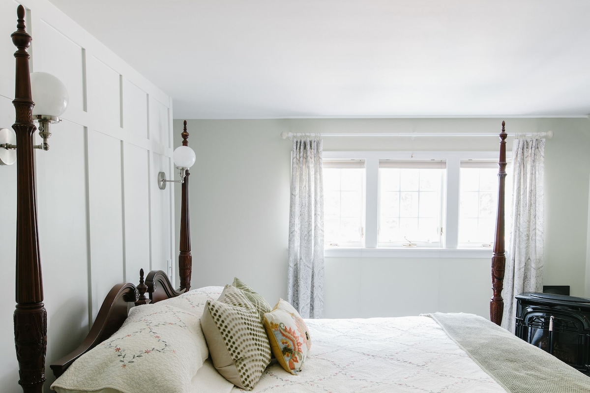 Ein Schlafzimmer mit Himmelbett, großem Fenster mit Vorhängen und Heizkörper.