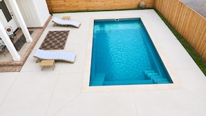 Ein rechteckiger Swimmingpool mit einer kleinen Whirlwanne, zwei Liegestühlen und einem kleinen Tisch.