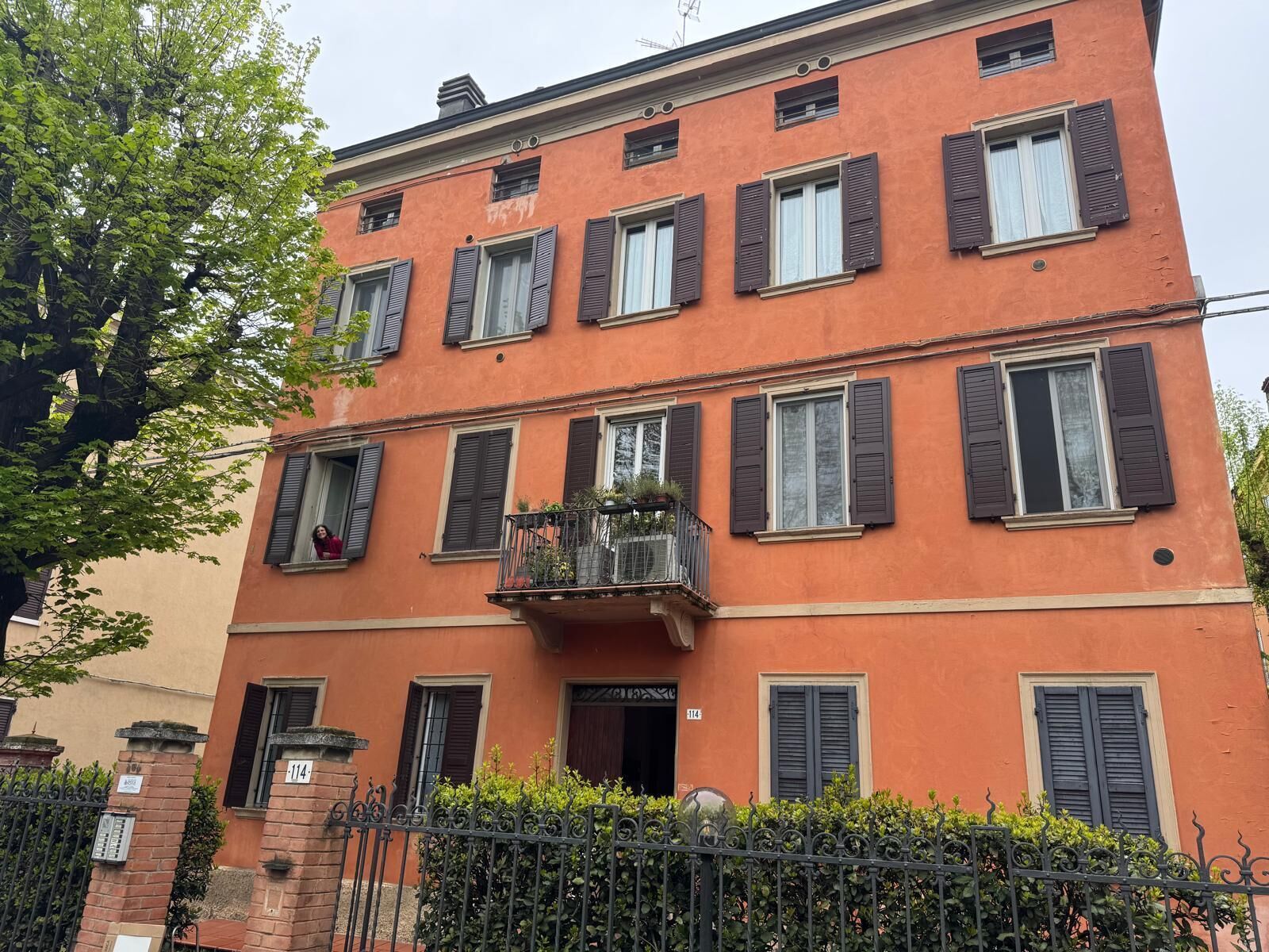 Un edificio a più piani con un balcone, un cancello in mattoni e un siepe.