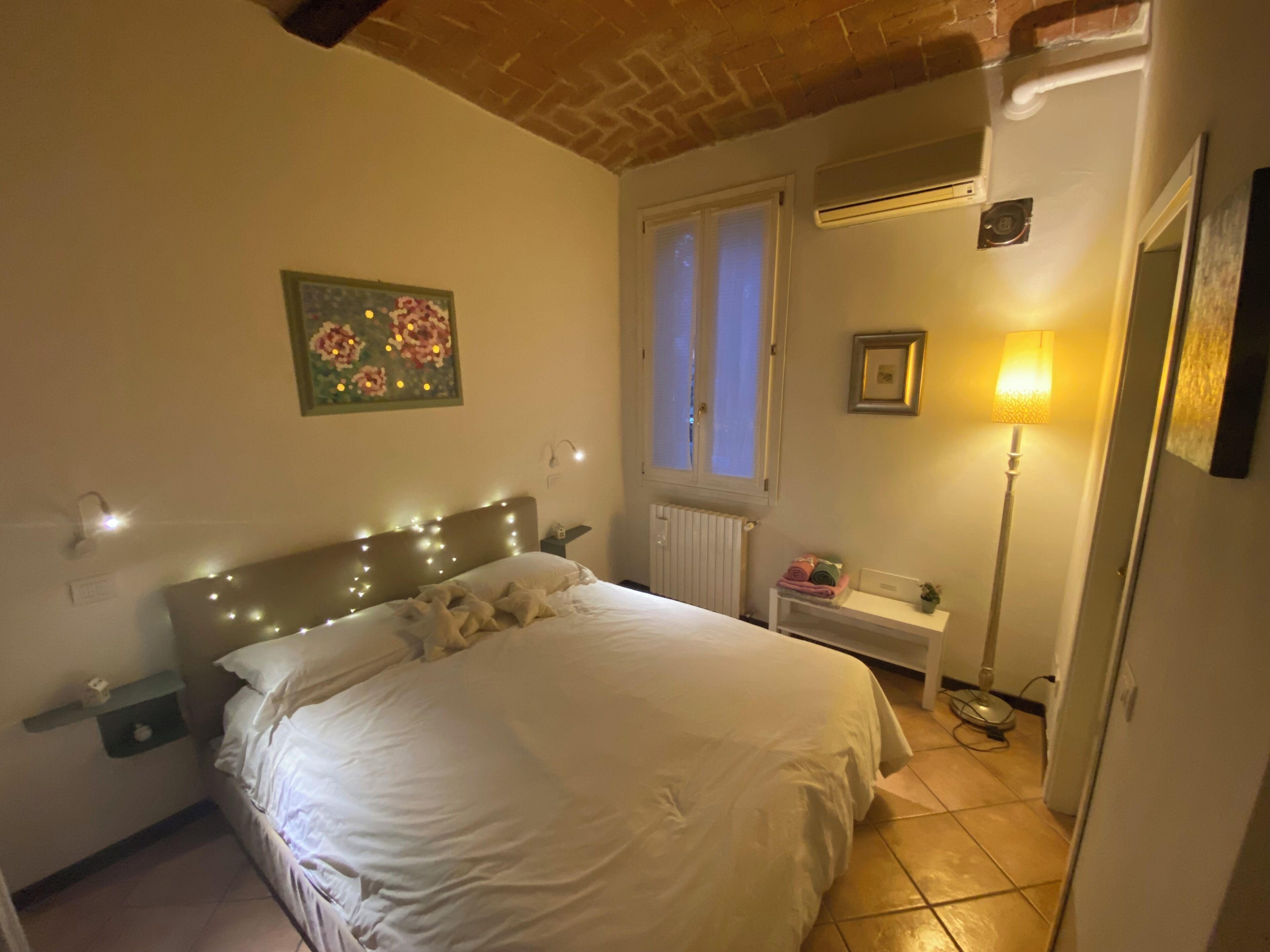 Una camera da letto con un letto, un comodino, una lampada e una finestra.