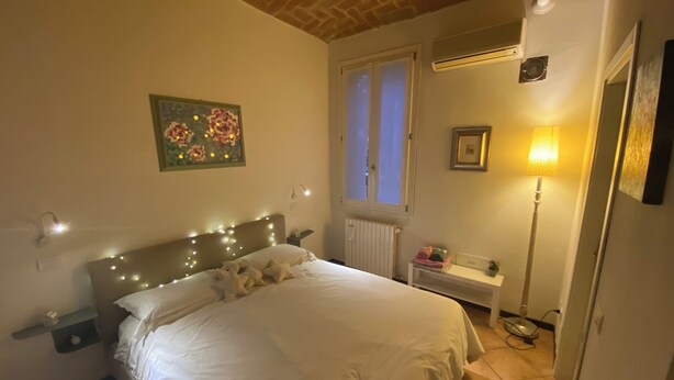 Un dormitorio con cama, mesita de noche, lámpara y ventana.