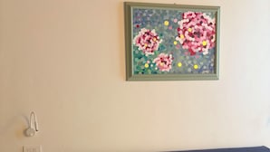 Un dormitorio con cama, almohadas, una mesita de noche, un interruptor de luz en la pared y una obra de arte enmarcada.