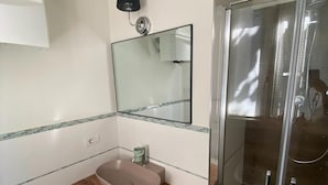 Un baño con tocador de madera, cabina de ducha de vidrio y espejo sobre el lavabo.