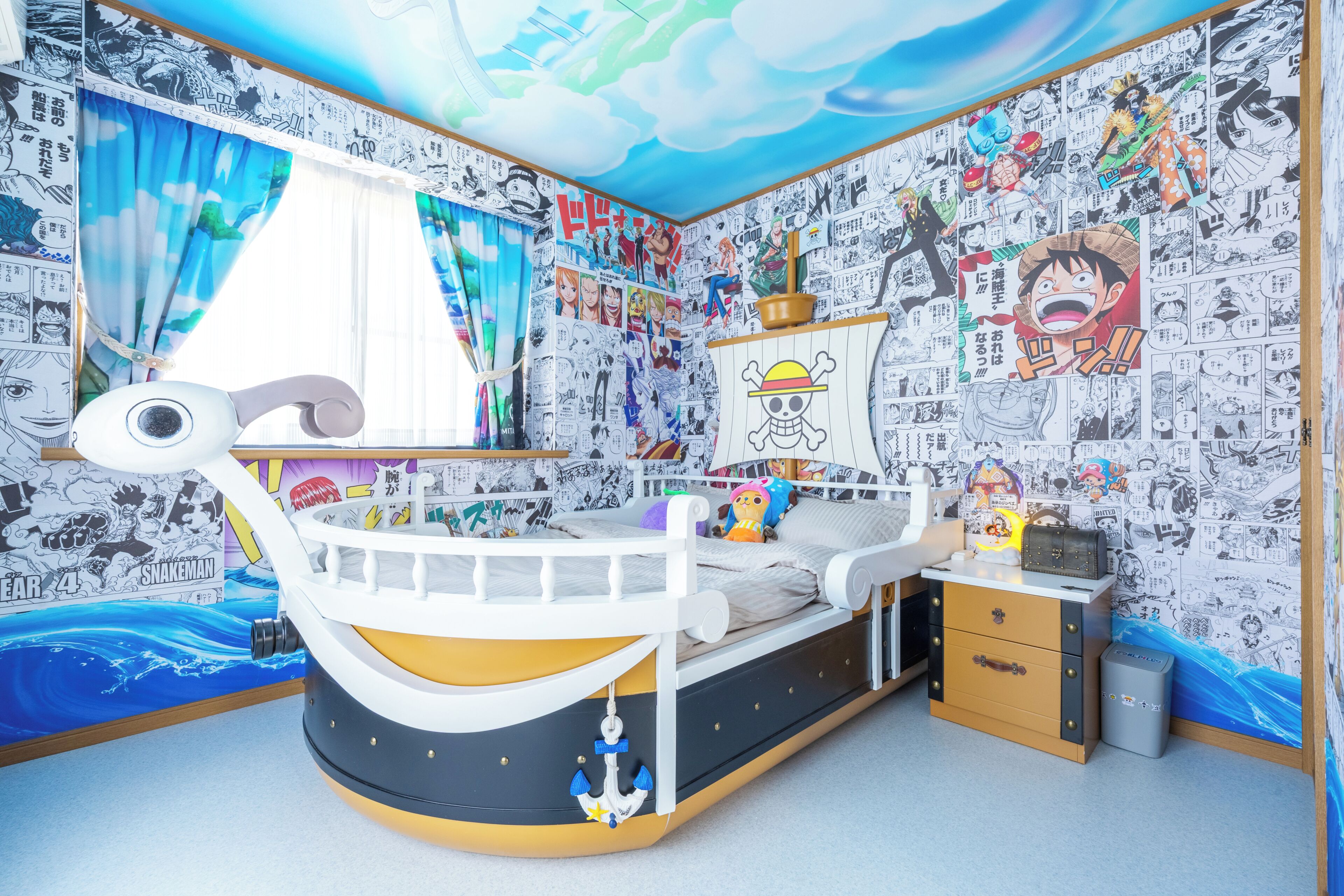 A room with a bed, a desk, and walls covered in manga-style artwork.