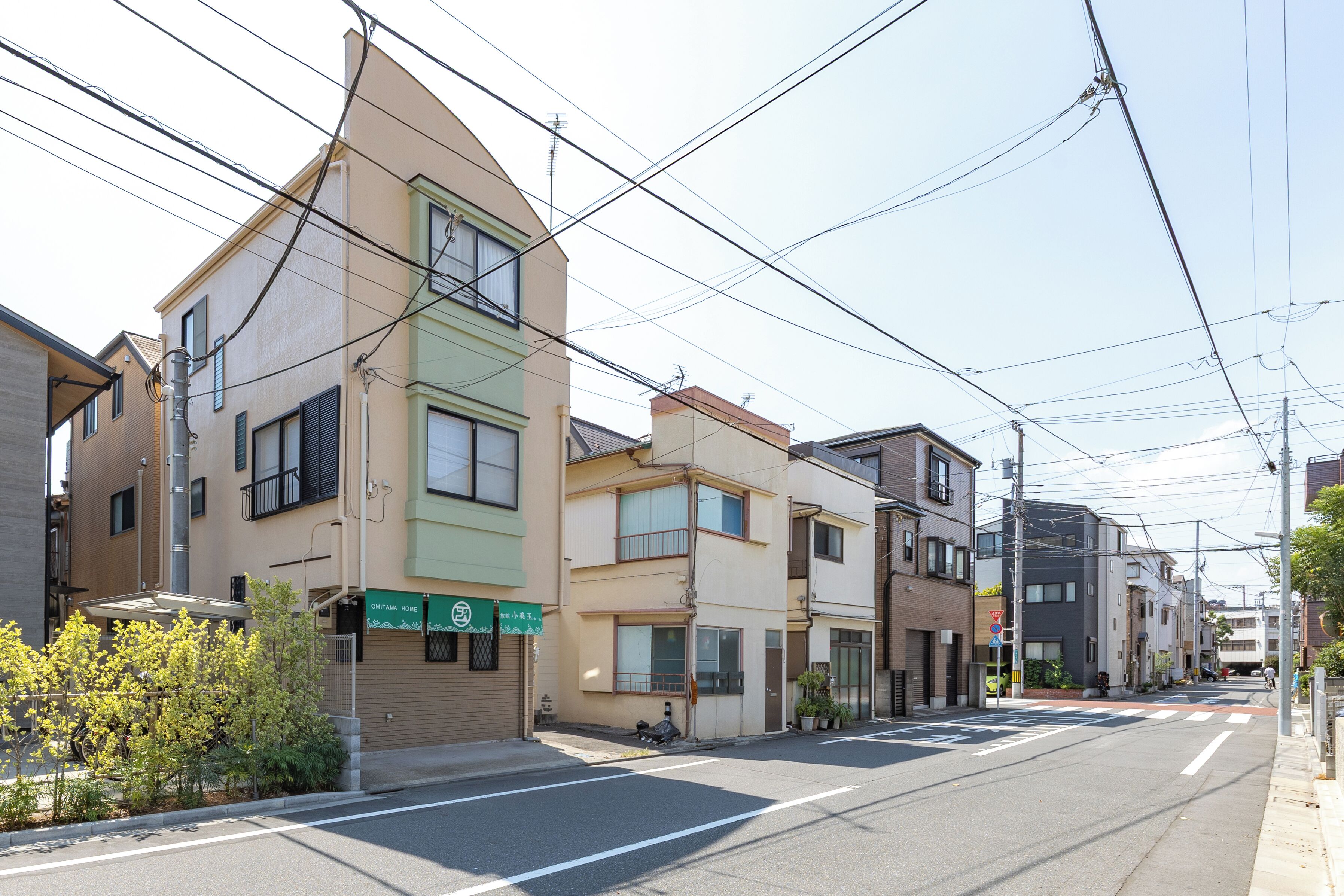 A residential street with multi-story buildings, a clear sky, and visible power lines.