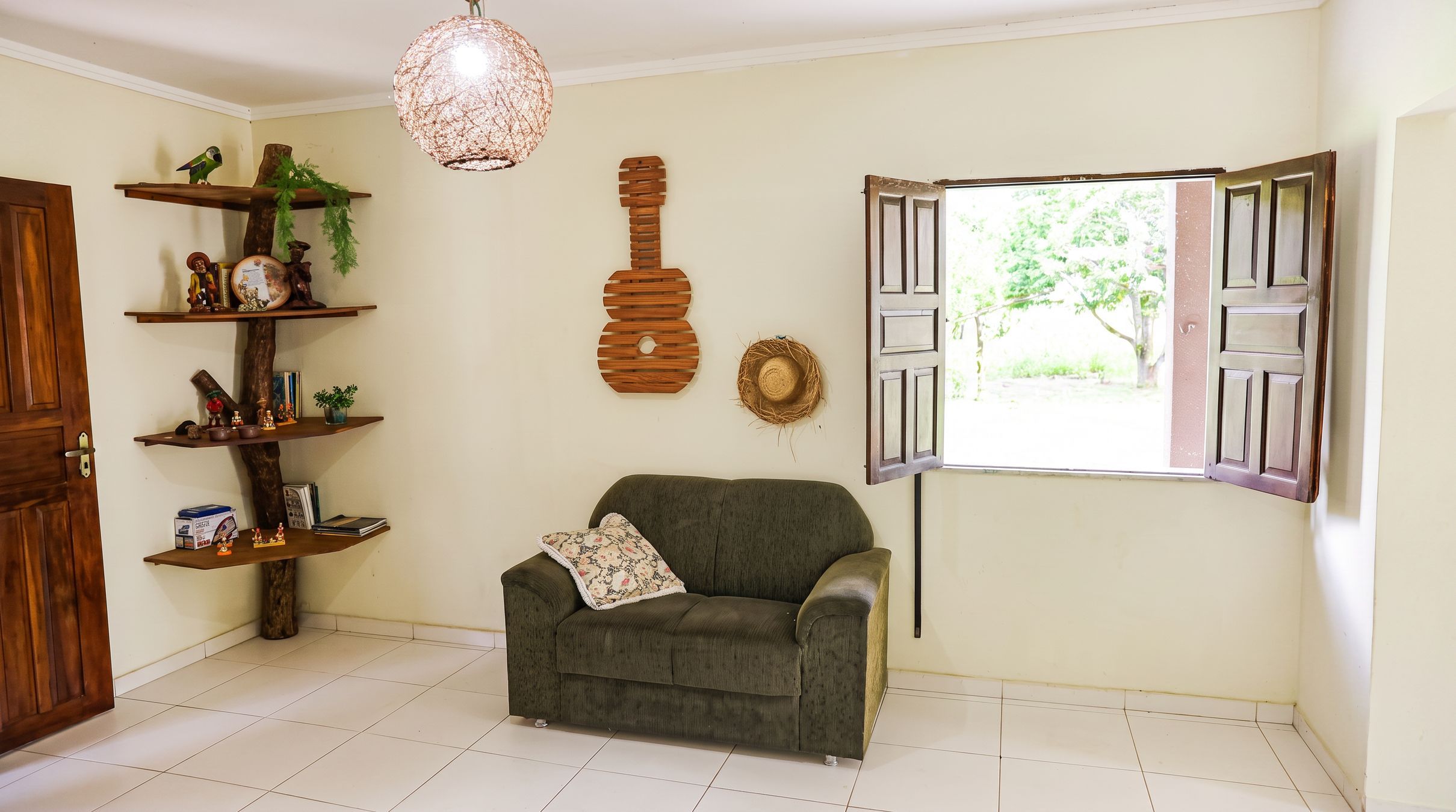 A living room with a sofa, a hanging light fixture, a wooden guitar decoration, and a window with open shutters.