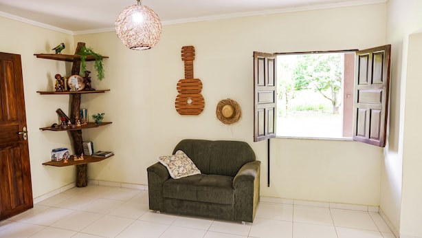 A living room with a sofa, a hanging light fixture, a wooden guitar decoration, and a window with open shutters.