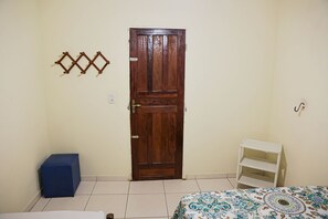 A room with a wooden door, a blue bench, a patterned bedspread, and a white shelf unit.