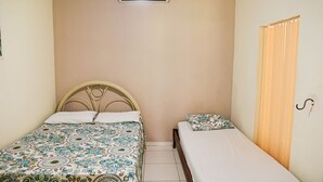 A bedroom with two beds, one larger and one smaller, a ceiling fan, and a window with curtains.
