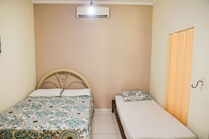 A bedroom with two beds, one larger and one smaller, a ceiling fan, and a window with curtains.