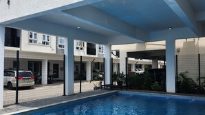 A swimming pool with a clear blue water surface, surrounded by a covered area with white pillars and a netted fence. - 2-Bedroom Duplex in Lekki, with 24/7 Light, Pool, Gym, and Playground. (Lekki)