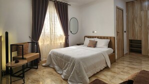 A bedroom with a bed, a nightstand, a chair, a window with curtains, a mirror, and a wardrobe. - 2-Bedroom Duplex in Lekki, with 24/7 Light, Pool, Gym, and Playground. (Lekki)