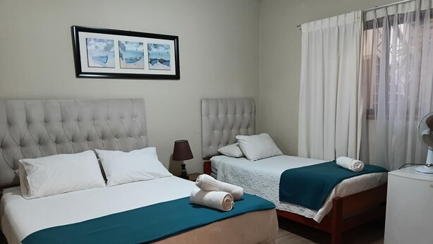 Une chambre d’hôtel avec deux lits, une table de chevet, une lampe et une fenêtre avec des rideaux.