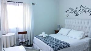 Une chambre d’hôtel avec un lit, une chaise, une table et une fenêtre avec des rideaux.