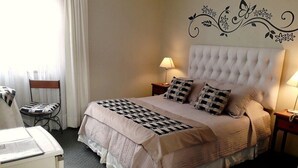 Une chambre d’hôtel avec un grand lit, deux tables de chevet avec des lampes, une chaise et un bureau avec une lampe.