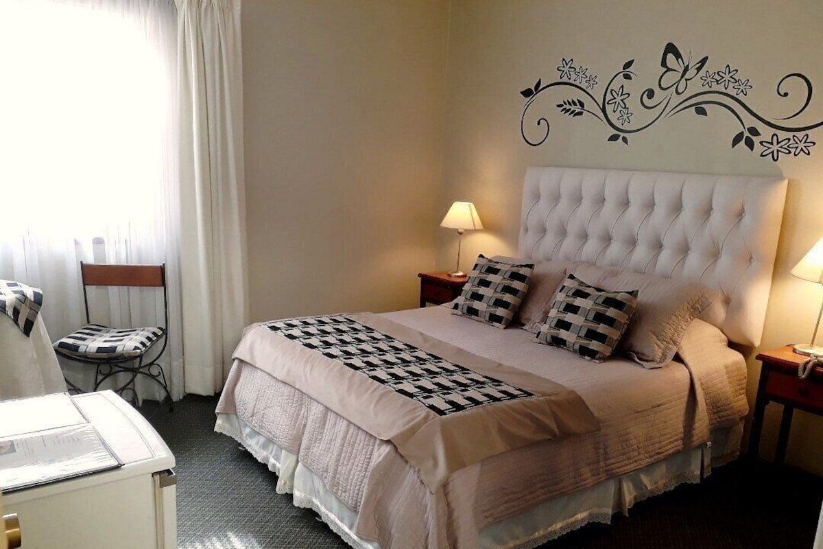 A hotel room with a large bed, two bedside tables with lamps, a chair, and a desk with a lamp.