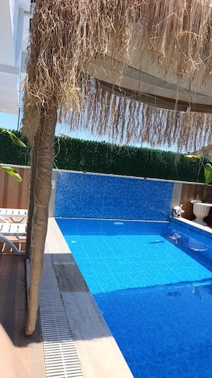 A swimming pool with a blue tiled edge, a palm tree, and a hedge in the background. - Stunning 2-Bedroom Villa with Heated Pool & Jacuzzi in Antalya, Kemer (Antalya)