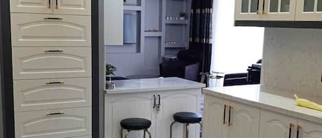 A modern kitchen with white cabinetry, a marble countertop, and a black and gray rug.