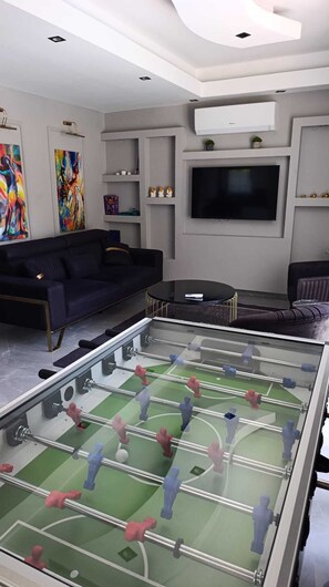 Un saló amb una taula de futbolí, un sofà, una televisió i obres d'art a les parets.
