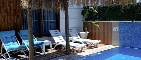 A swimming pool with lounge chairs and a covered area with a thatched roof.