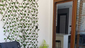 Une table à plateau en verre, une chaise en osier, une plante fixée au mur et une porte-fenêtre coulissante donnant sur une pièce.