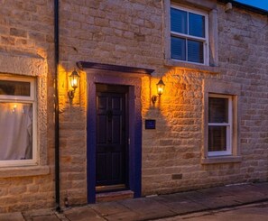 A stone building with a dark blue door, two windows with white frames, and two wall-mounted lights. - Spa Cottage - Hot tub, Cold Pod & Sauna (Morecambe)