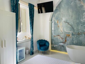 A modern bathroom with a marble wall, a large bathtub, and a blue chair. - Nestled among the rows of orange trees, Zagara Suite is an oasis of peace and relaxation (Francofonte)