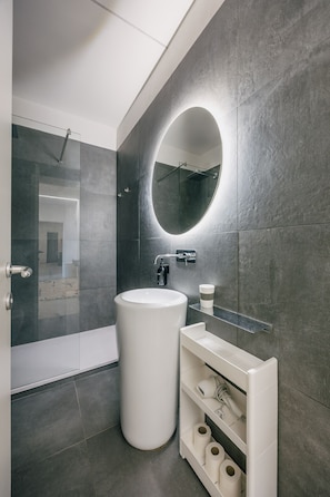 A modern bathroom with a large round mirror, a white sink, and a glass shower enclosure. - Vrbo Property (Arezzo)