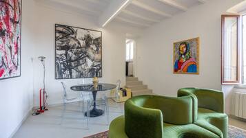 Un soggiorno moderno con un tavolo rotondo in vetro, sedie trasparenti, un divano verde e opere d'arte alle pareti.