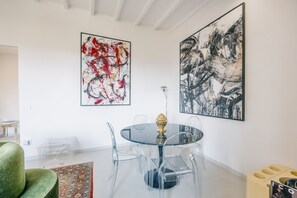 A modern dining area with a glass table and chairs, a green sofa, and two large abstract paintings on the walls. - Vrbo Property (Arezzo)