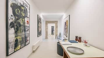 Un corridoio con opere d'arte alle pareti, un tavolo con libri e un oggetto decorativo, e una porta in fondo.