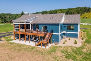 A two-story house with a covered patio, outdoor seating, and a small garden area. - New! Luxurious Lake Access Getaway w/ Indoor Pool (Swanton)