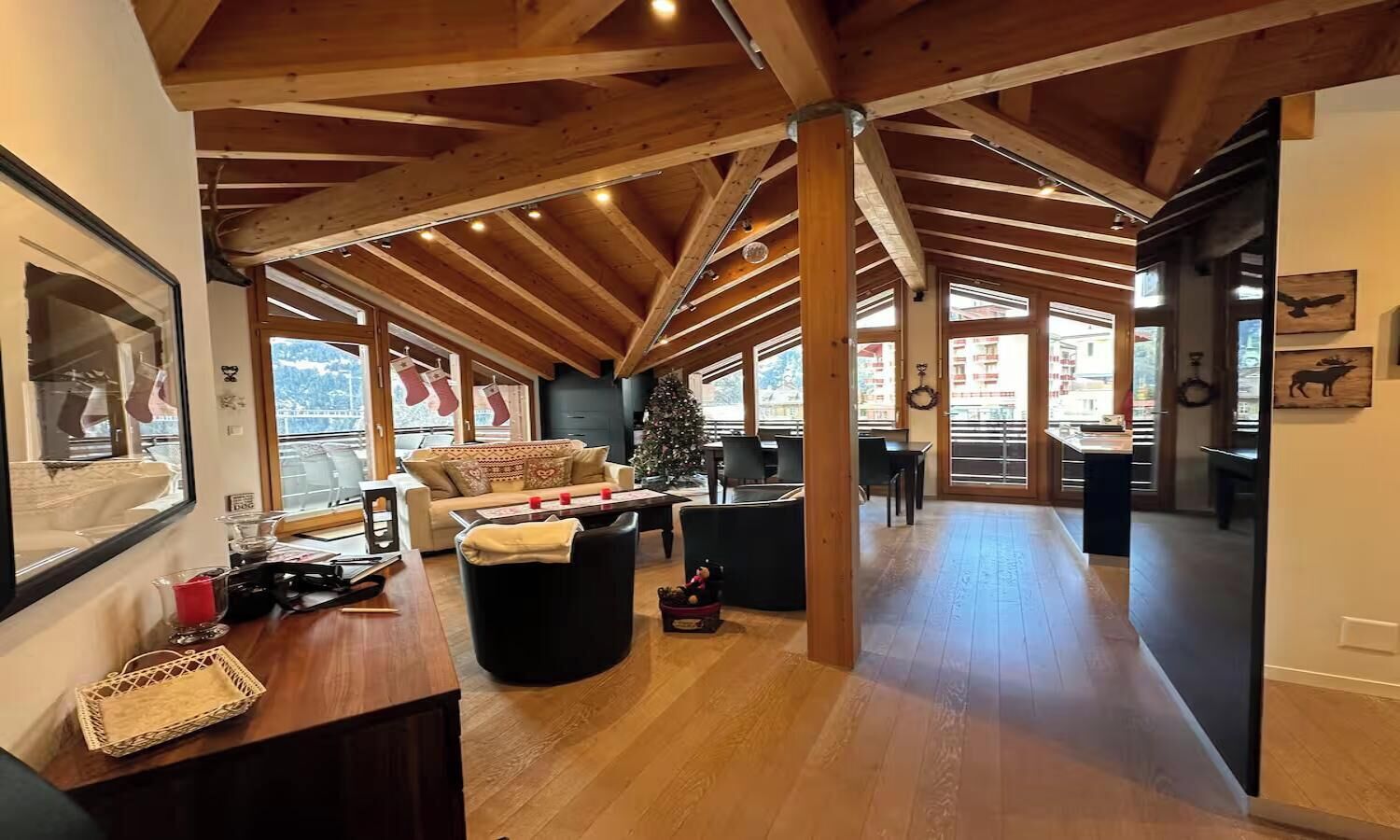 Un amplio espacio habitable con techo alto y vigas de madera, una zona de estar acogedora y vistas a través de grandes ventanales.