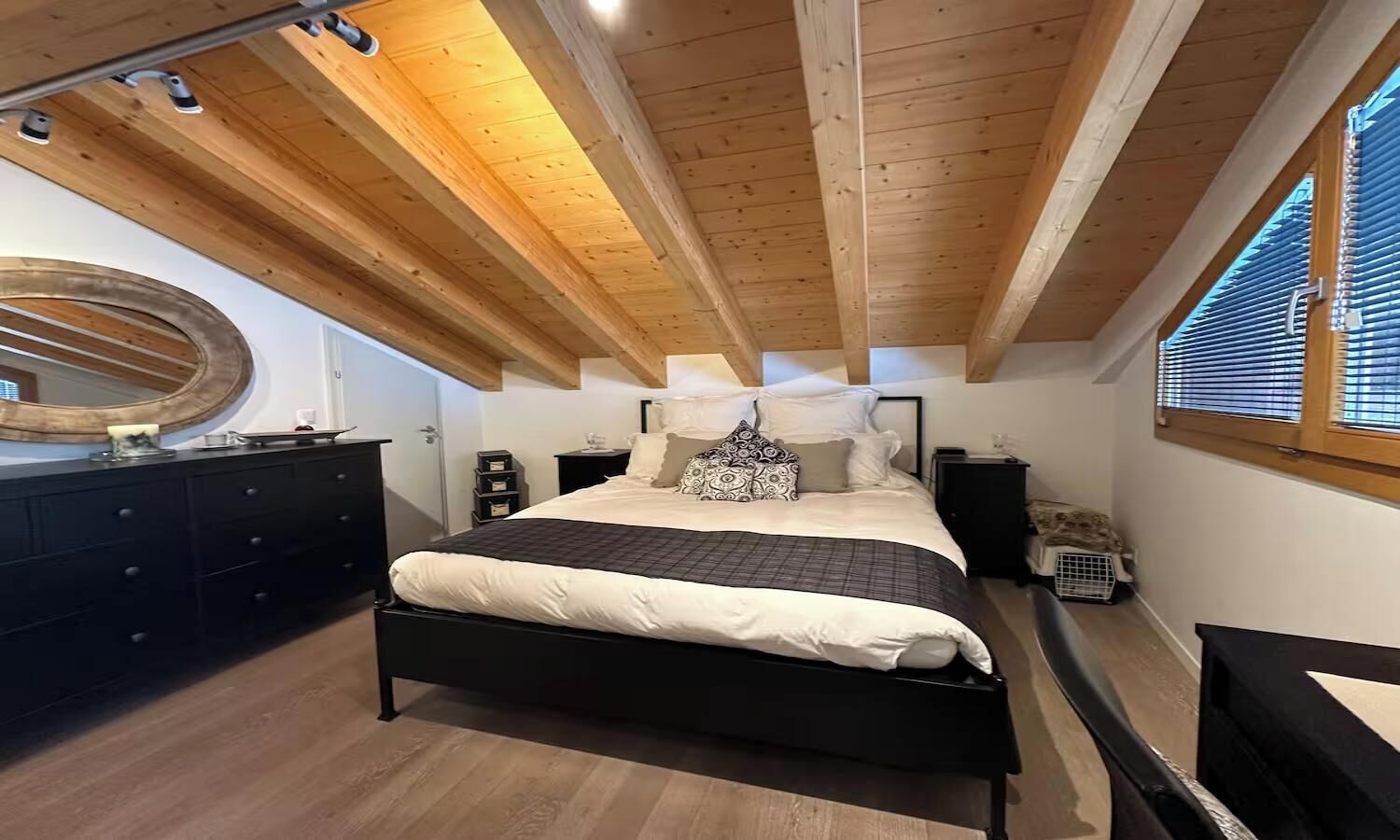 A bedroom with a bed, bedside tables, a dresser, a mirror, and a window with blinds.