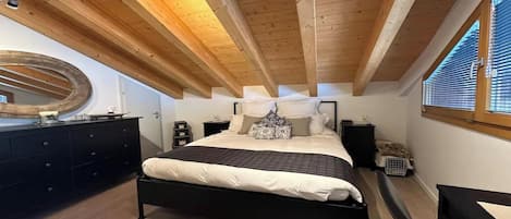 A bedroom with a bed, bedside tables, a dresser, a mirror, and a window with blinds.