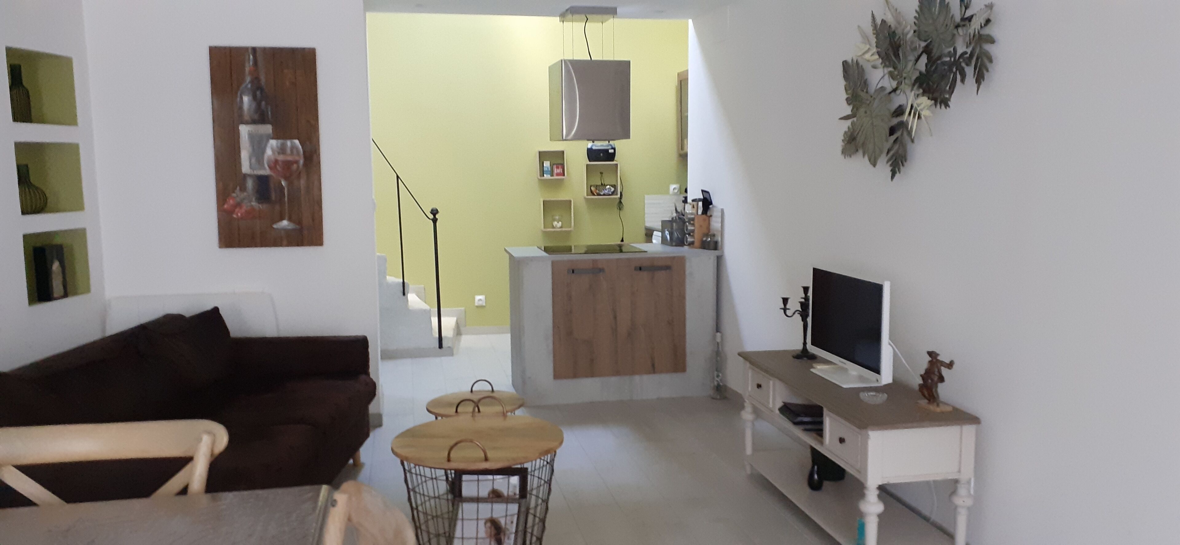 Una sala de estar con un sofá marrón, una mesita redonda y un televisor sobre un soporte blanco.