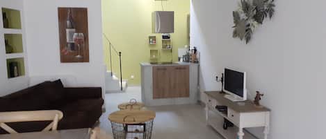 Sala de estar com sofá marrom, mesa redonda pequena e televisão sobre um suporte branco.